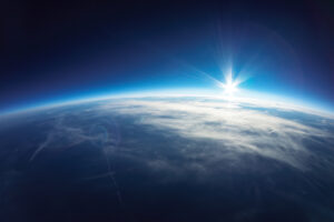 View of Earth from space with the sun rising over the horizon, casting a bright light and illuminating the atmosphere.