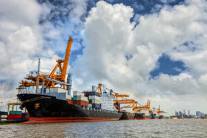 Cargo ships with containers docked at a port under a cloudy sky, with cranes ready for unloading.