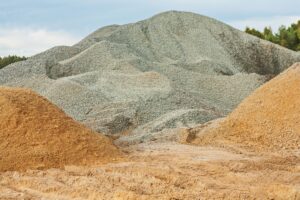 Piles of gravel and sand in a construction site with trees in the background.