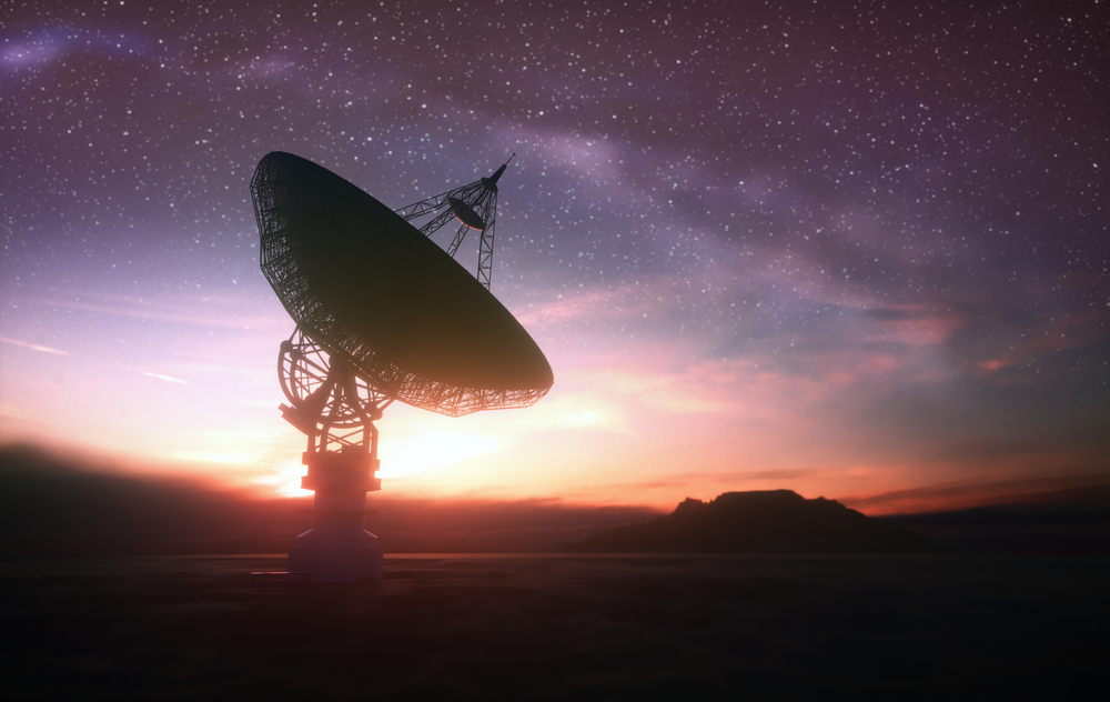 A large satellite dish silhouetted against a colorful sunset sky and starry background.