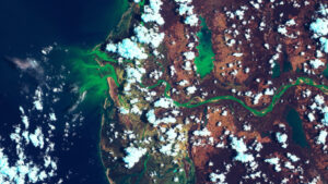 Aerial view of a vibrant green river winding through a landscape with patches of clouds and ocean.