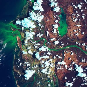 Satellite view of a landscape with green waterways, brown terrain, and scattered white clouds.