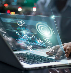 Person typing on a laptop with futuristic technology graphics, including graphs and gears, overlaid on the screen.