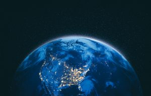 A bright Earth with illuminated cities is visible from space against a backdrop of a starry sky.