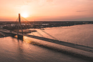 Sunset view of a suspension bridge over a calm river, with soft orange and pink hues in the sky.