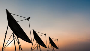 Three large satellite dishes silhouetted against a colorful sunset sky.