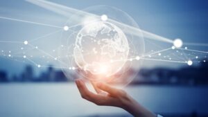 Hand holding a glowing digital globe with network lines against a blurred ocean and sky background.