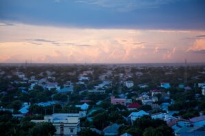Aerial view of a cityscape at sunset with scattered houses and trees under a colorful sky.