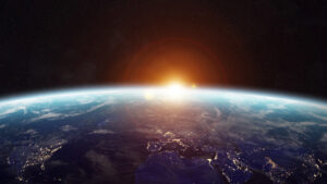 Sunrise over Earth as seen from space, with the sun's light illuminating the planet's horizon and visible city lights.