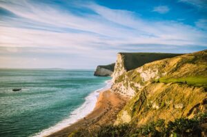 Cliffs overlooking a beach and the sea under a clear blue sky, with waves gently lapping the shore.