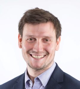 Smiling man in a suit with a collared shirt, against a plain white background.