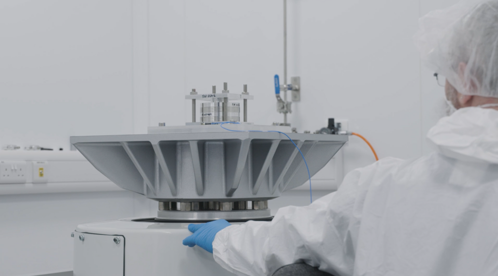 Person in lab coat and gloves operates industrial equipment in a sterile room.
