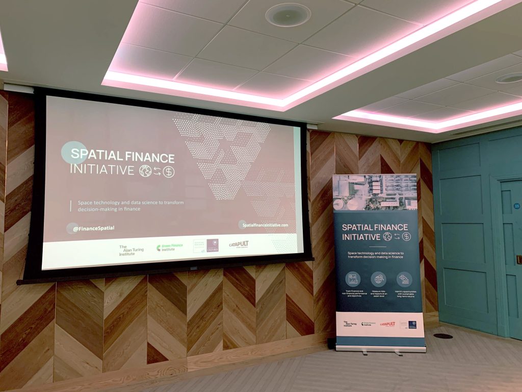 Conference room with a presentation screen and a standing banner for the Spatial Finance Initiative.