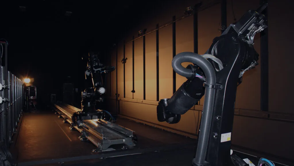 Two large robotic arms on tracks in a dimly lit industrial or laboratory setting.