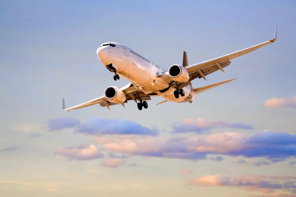 A commercial airplane flying in the sky with scattered clouds at sunset.