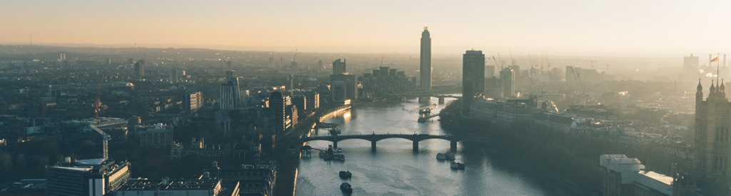 Aerial view of a city skyline at sunrise, featuring a river with several bridges and tall buildings.