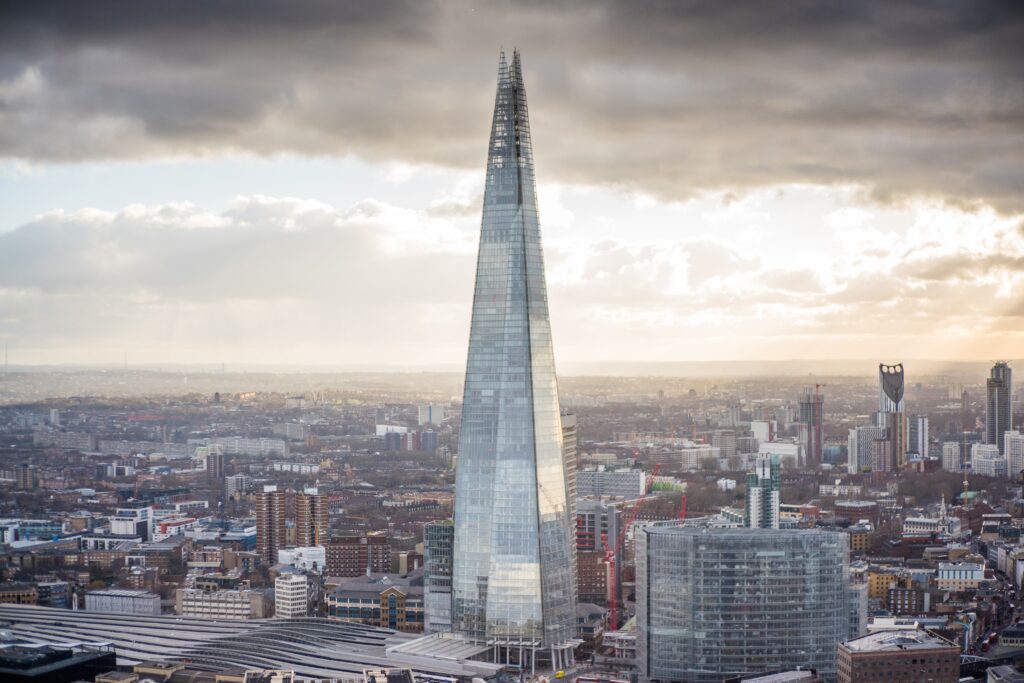 The Shard skyscraper in London stands tall against a cloudy sky, with the cityscape in the background.