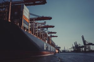 Large cargo ship docked at a port with cranes and shipping containers under a clear blue sky.