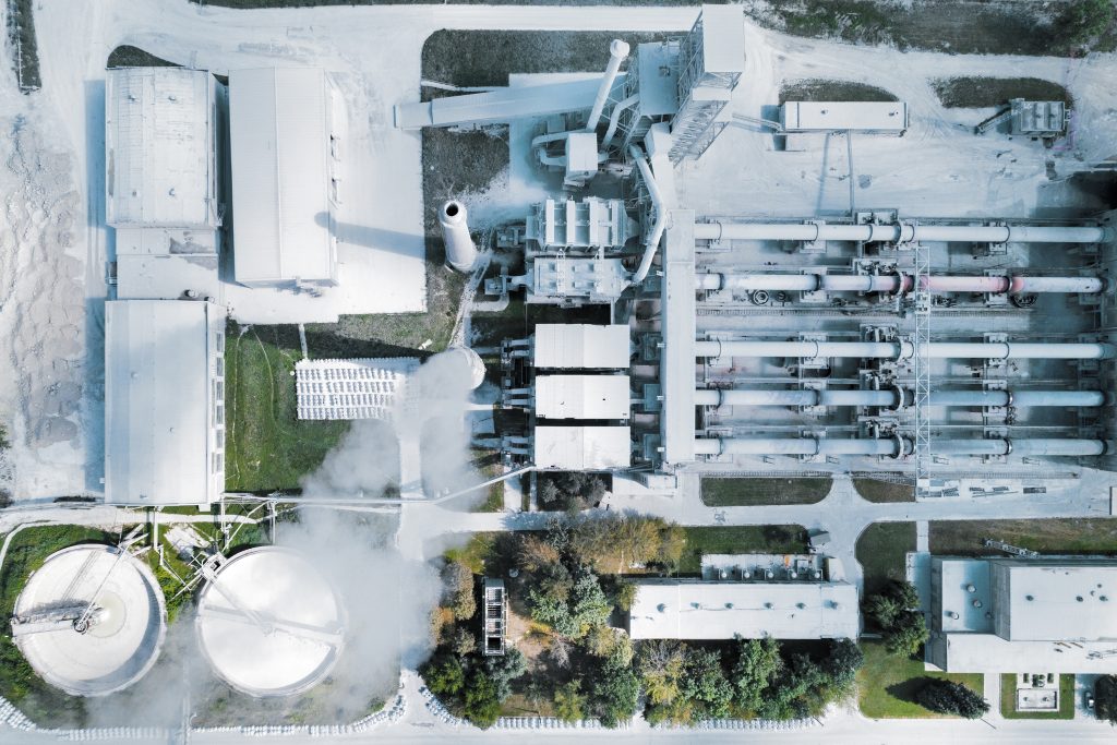 Aerial view of an industrial complex with buildings, silos, pipes, and surrounding greenery.
