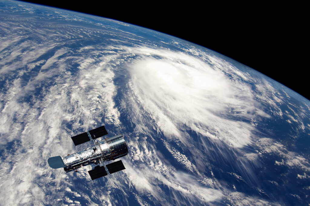 Satellite orbiting Earth with a swirling storm visible over the ocean in the background.