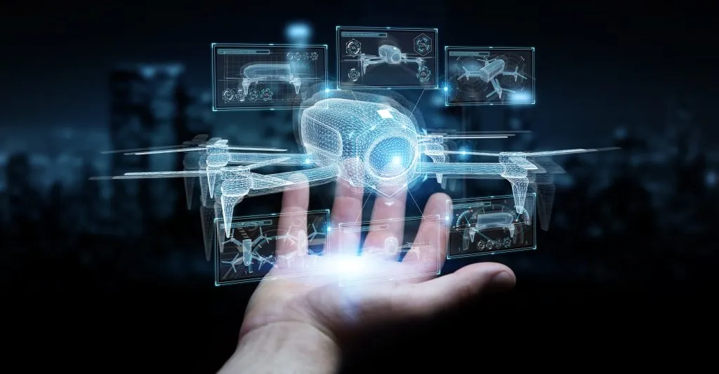A hand holds a glowing digital hologram of a drone with multiple technical interface screens around it.