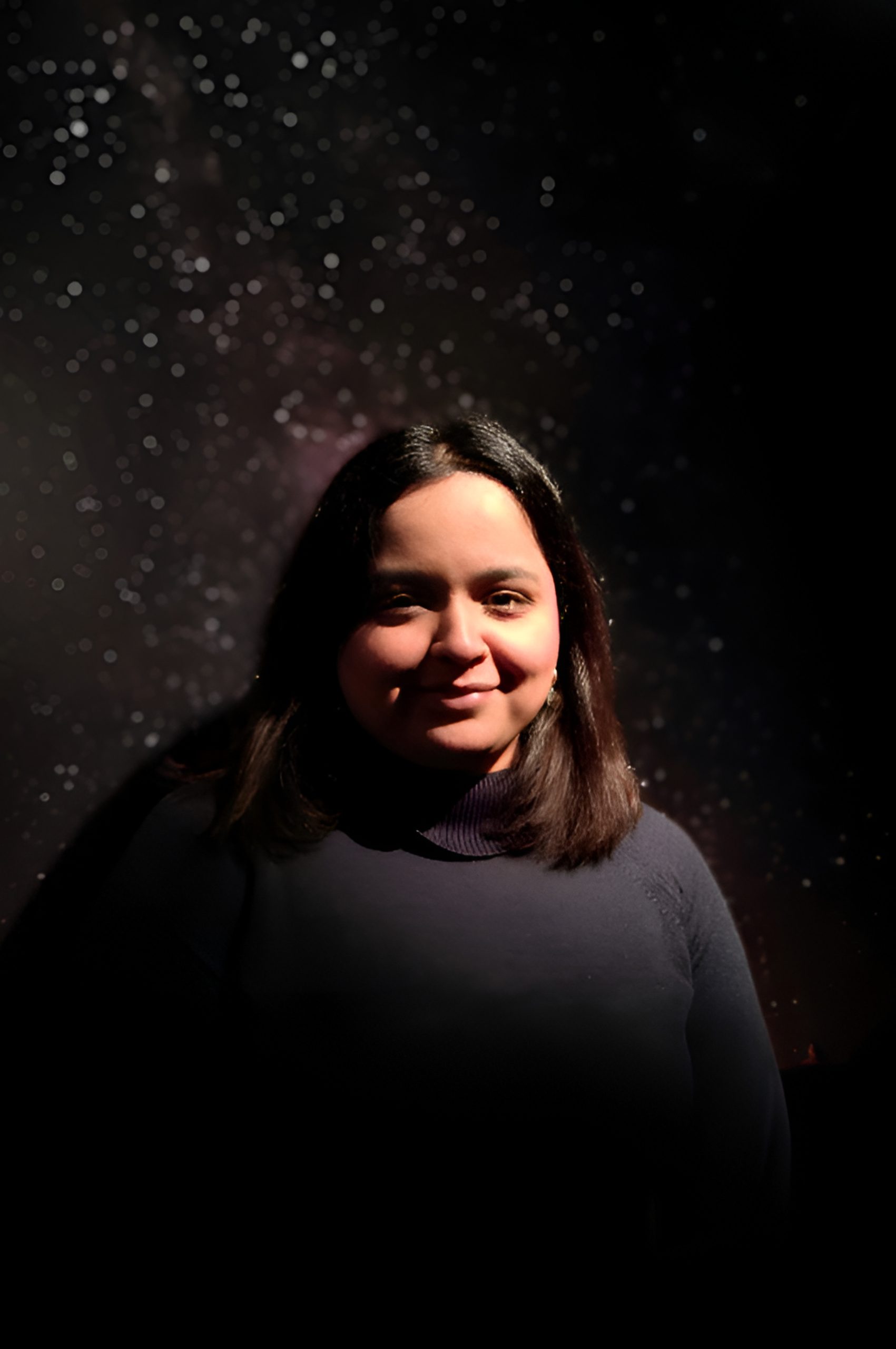 A woman with dark hair smiles softly, standing against a starry night sky background.