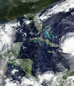 Satellite image of a hurricane approaching the Caribbean with clouds swirling over the ocean and surrounding land.