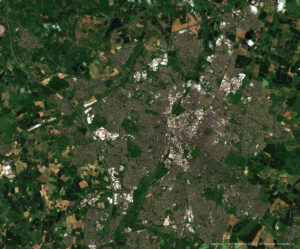 Satellite view of a city surrounded by green fields and scattered clouds.