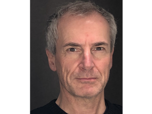 Man with short gray hair wearing a black shirt, looking directly at the camera.