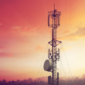 Telecommunications tower at sunset with a vivid orange and pink sky.