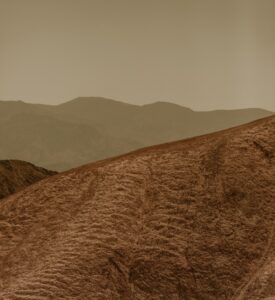 Arid desert landscape with rolling hills and distant mountain range under a hazy sky.