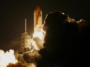 Space shuttle launching at night with bright flames and smoke billowing against a dark sky.