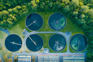 Aerial view of six circular water treatment tanks surrounded by lush green trees.
