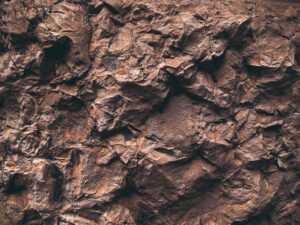 Close-up of a rugged, textured brown rock surface with various crevices and jagged features.