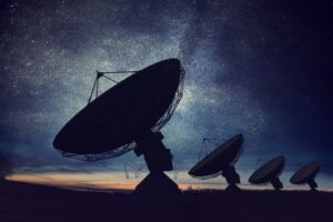 Silhouetted satellite dishes against a starry night sky, with a faint Milky Way in the background.