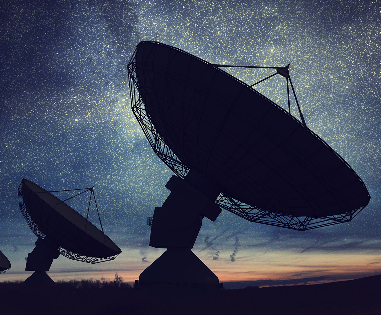 Silhouettes of large satellite dishes against a starry night sky, with a sunset glow on the horizon.