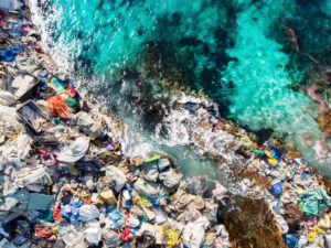 Aerial view of garbage along a turquoise ocean shoreline with waves crashing on the debris.
