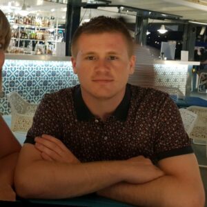 Man sitting at a bar with arms crossed, wearing a patterned shirt, and looking at the camera.