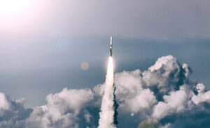 Rocket launching into a cloudy sky with a trail of smoke and bright sunlight in the background.