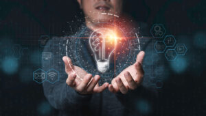 Hands holding a glowing digital light bulb with tech icons and a circuit board background.