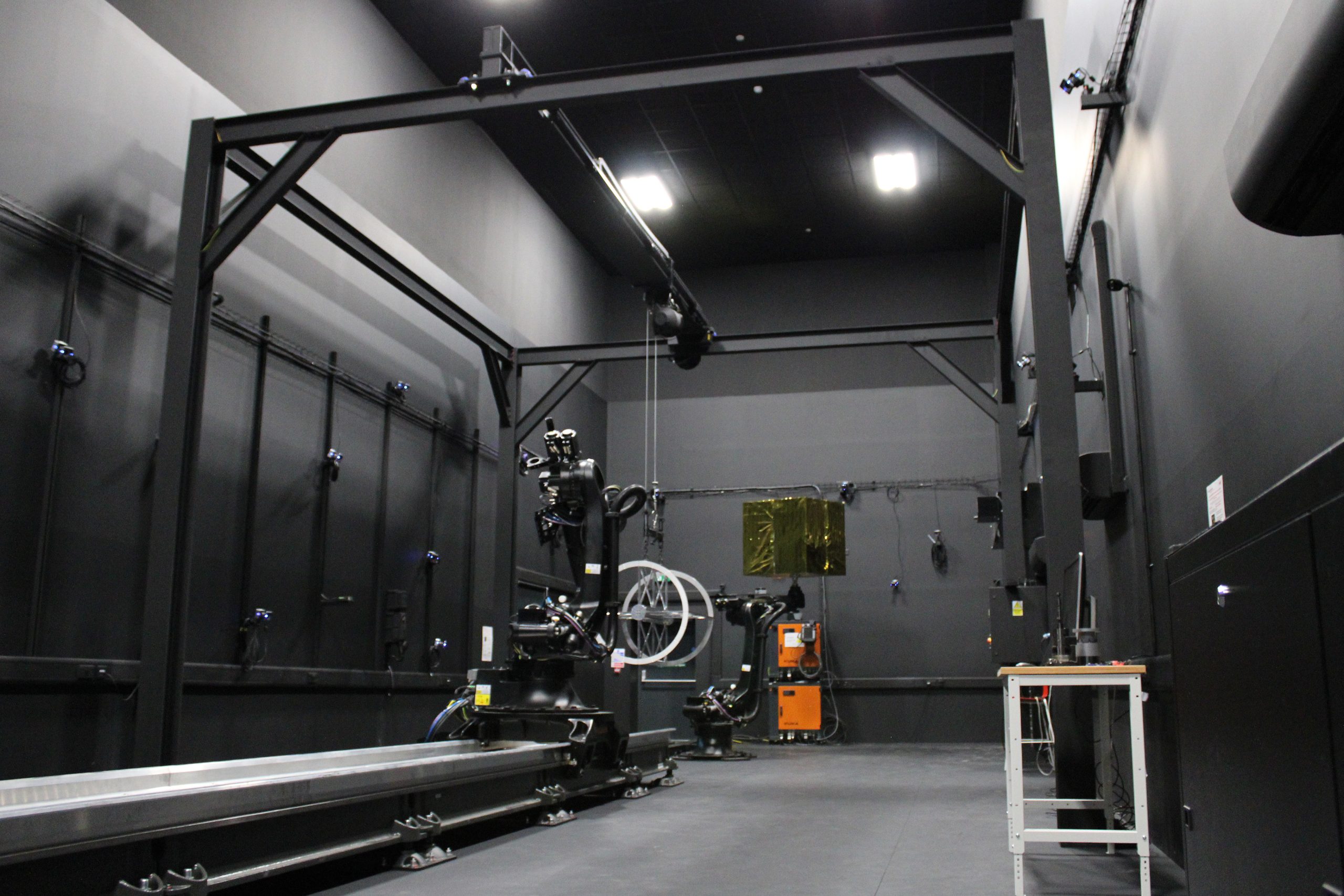 A high-tech lab with robotic equipment, black walls, and overhead lighting.