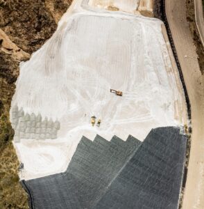 Aerial view of a construction site with earthmoving equipment on a large, partially covered area near a road.