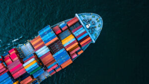 Aerial view of a cargo ship loaded with multicolored containers sailing on dark blue water.