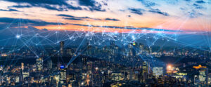 A city skyline at sunset with digital network lines connecting buildings, symbolizing connectivity and technology.
