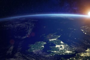 View of Earth from space, showing the British Isles at night with city lights and the sun rising over the horizon.