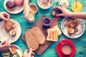 Breakfast table with bread, spreads, eggs, pastries, fruit, juice, milk, and coffee on a blue wooden surface.