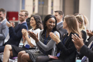 Audience clapping and smiling during a presentation or event in a conference room.