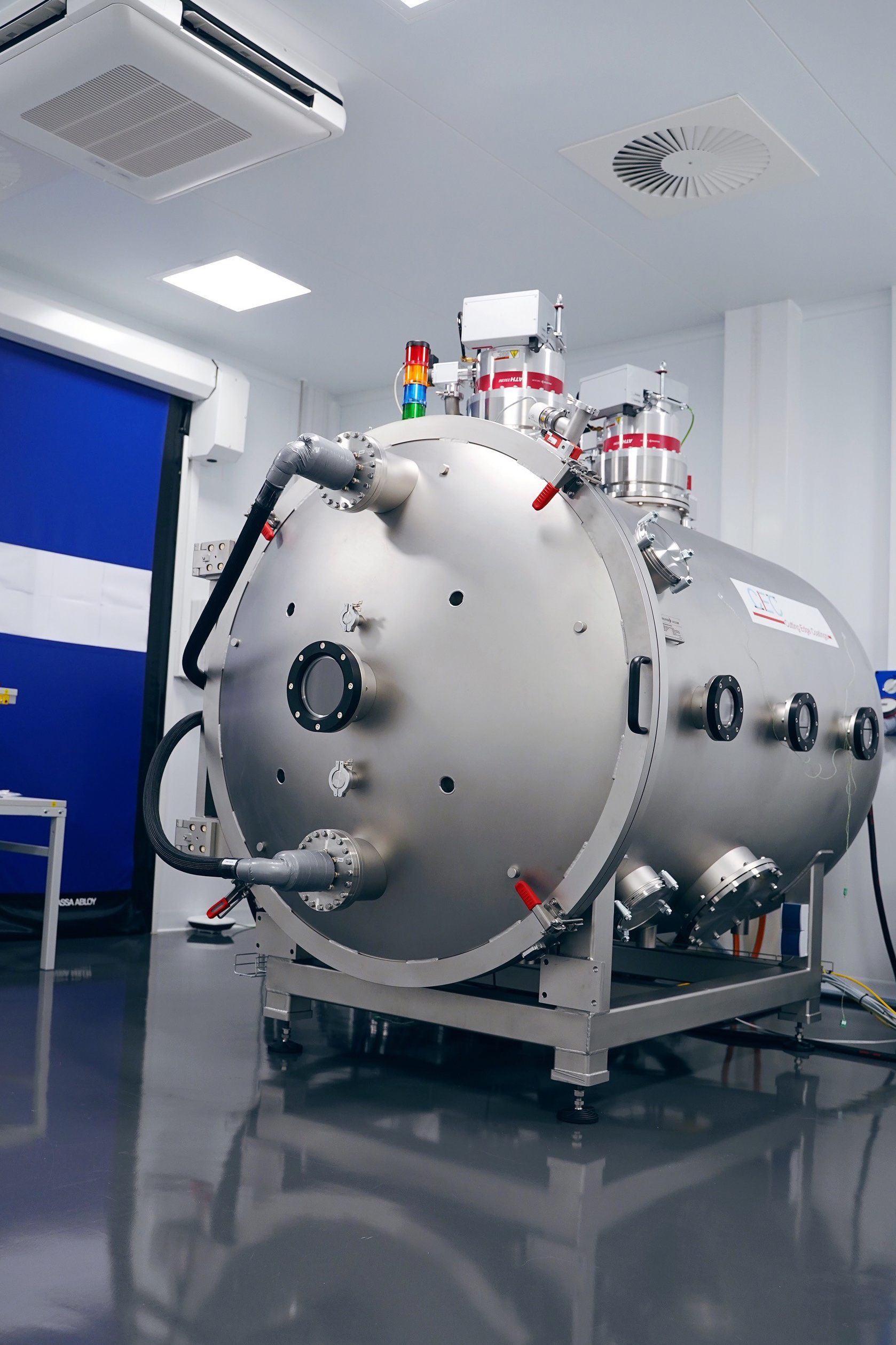 Large industrial metal chamber with multiple valves and cables in a clean laboratory setting.