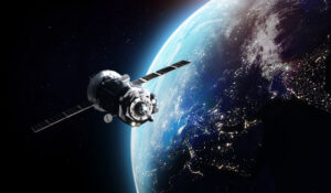 A satellite orbits Earth with city lights visible on the darkened surface and the sun illuminating the planet's edge.
