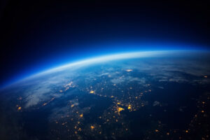 View of Earth from space showing city lights and a blue atmospheric glow on the horizon.